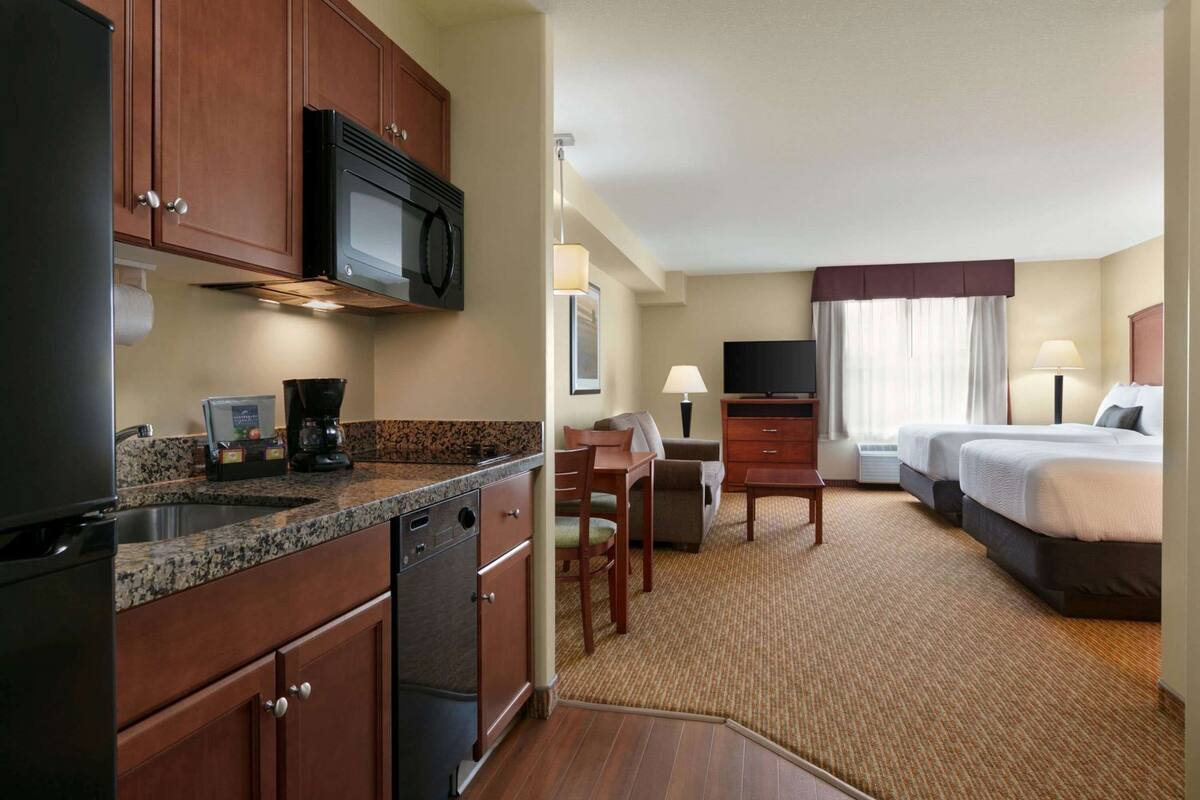 Habitación de hotel con kitchenette, cama, escritorio y televisor.