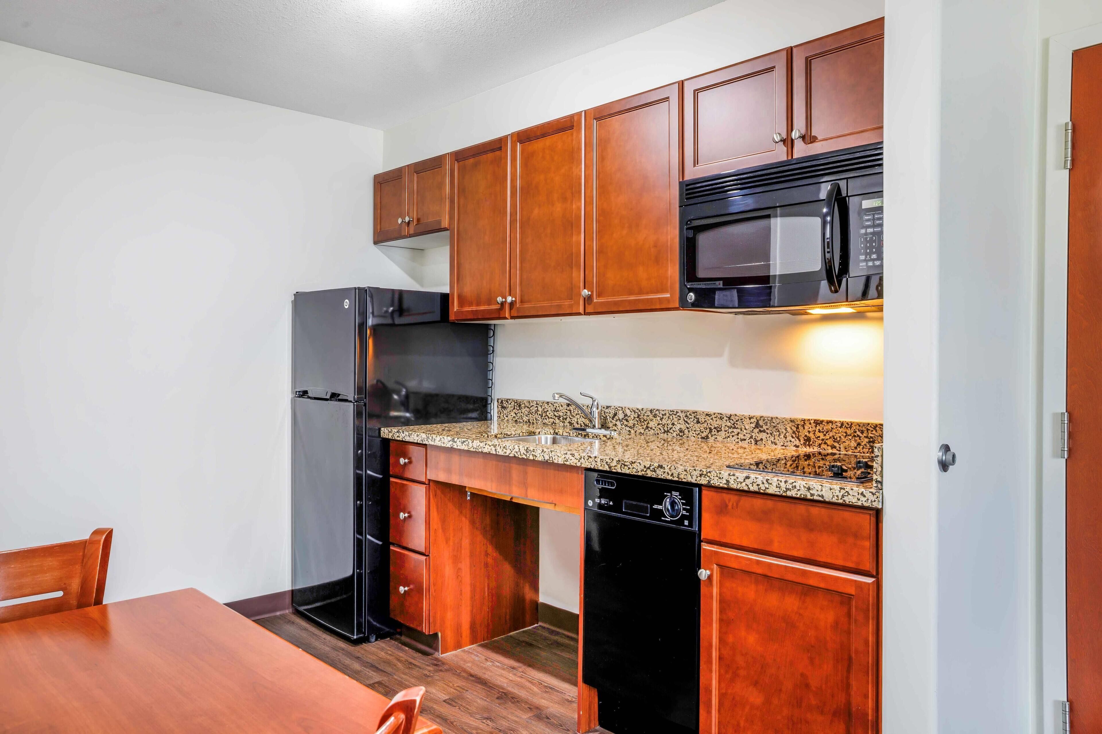 Una cocina compacta con armarios de madera, un refrigerador negro, un microondas y un lavavajillas.