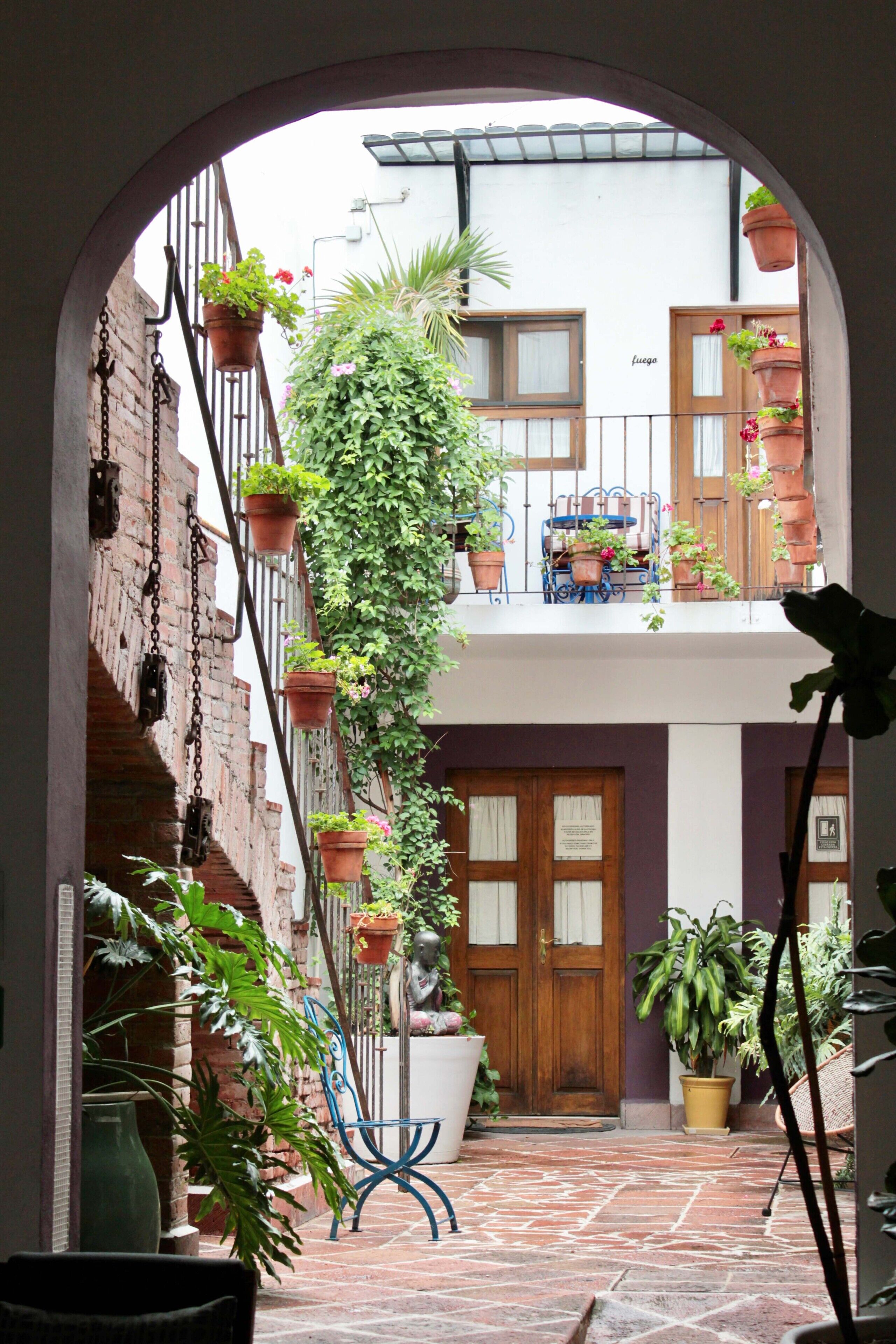 A courtyard with a brick wall, hanging planters, a blue metal bench, and a wooden door.
