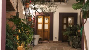 Un patio con piso de piedra, plantas en macetas, una puerta de madera y una bicicleta.