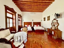 A hotel room with two beds, a wooden ceiling, a sitting area with a table, and a dresser.