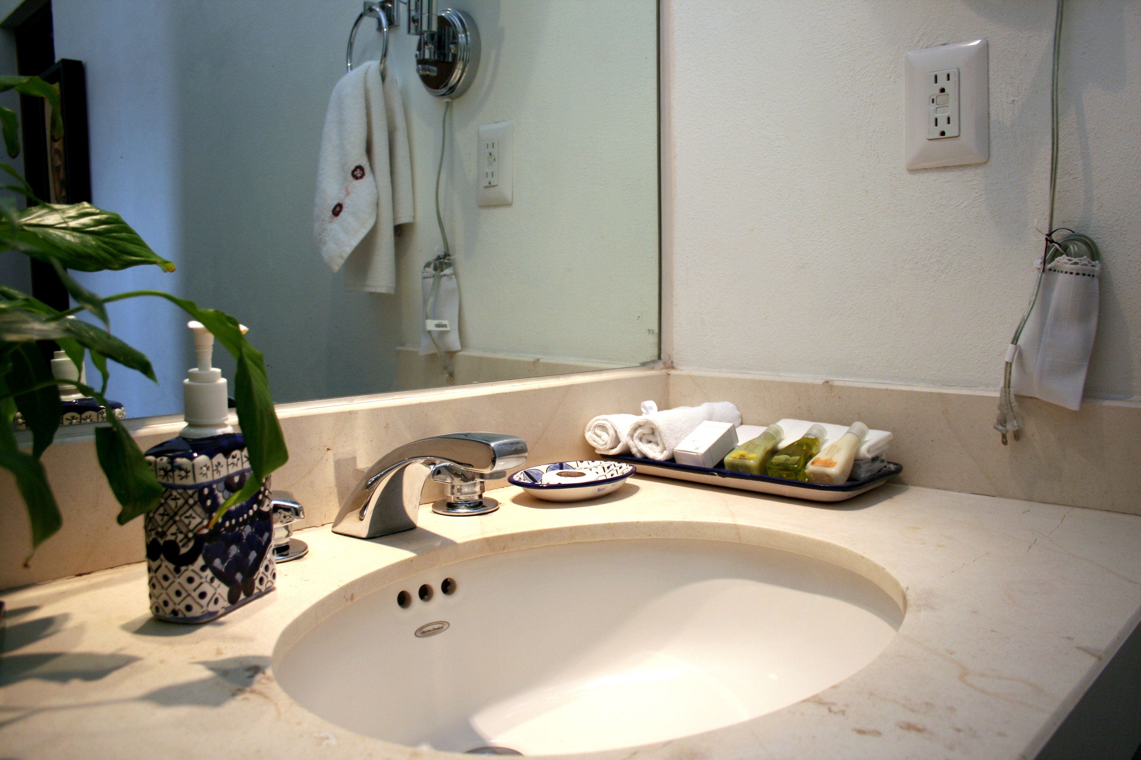 A bathroom with a sink, faucet, and a mirror. There are towels and toiletries on the counter.