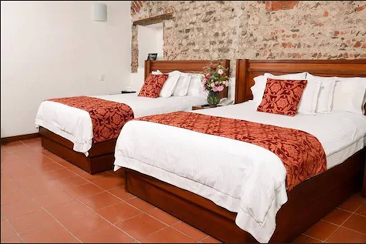 Two double beds with wooden frames and red patterned bedspreads, a floral wall decoration, and a tiled floor.