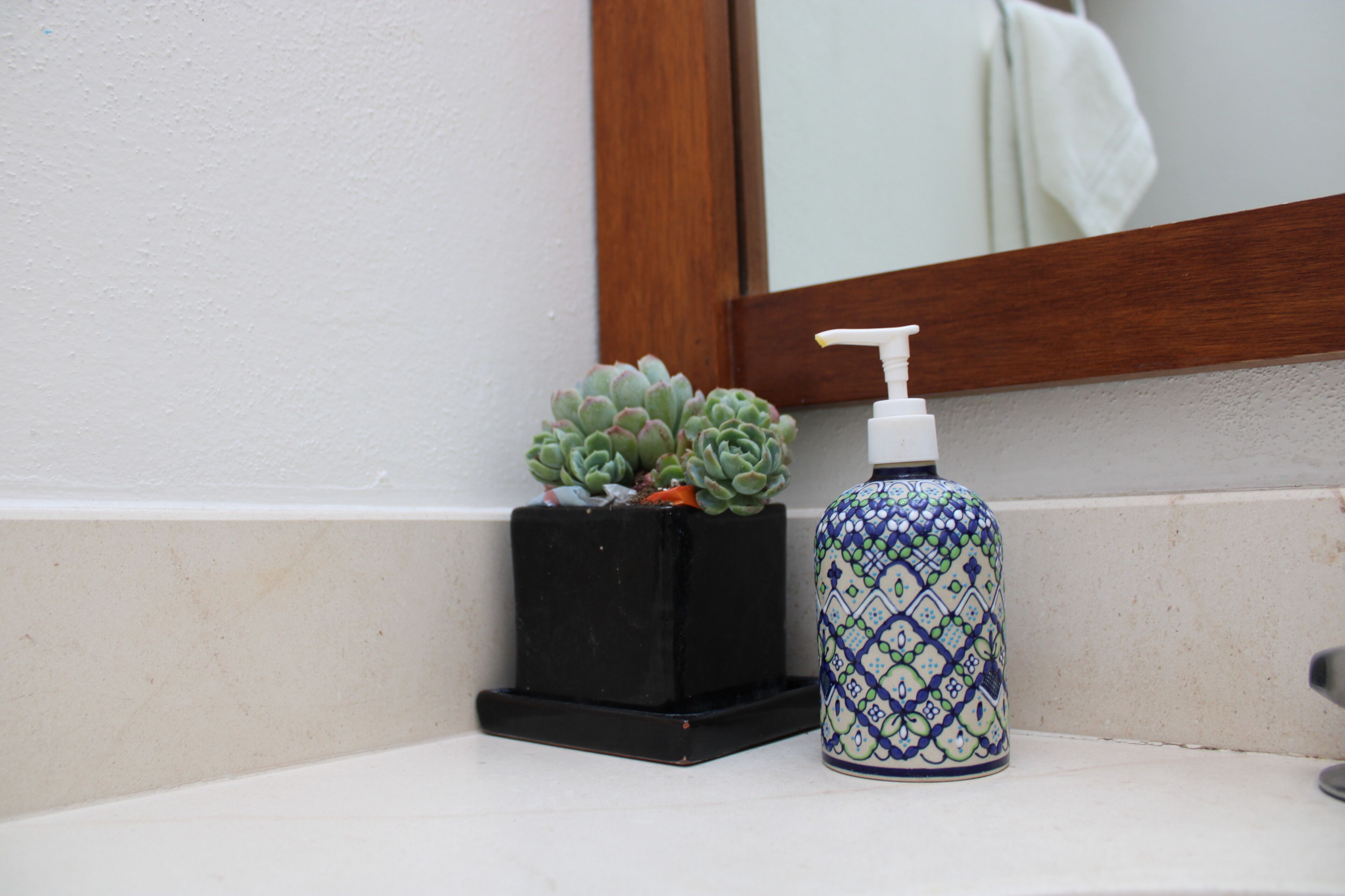 A bathroom sink with a black soap dispenser and a decorative vase.