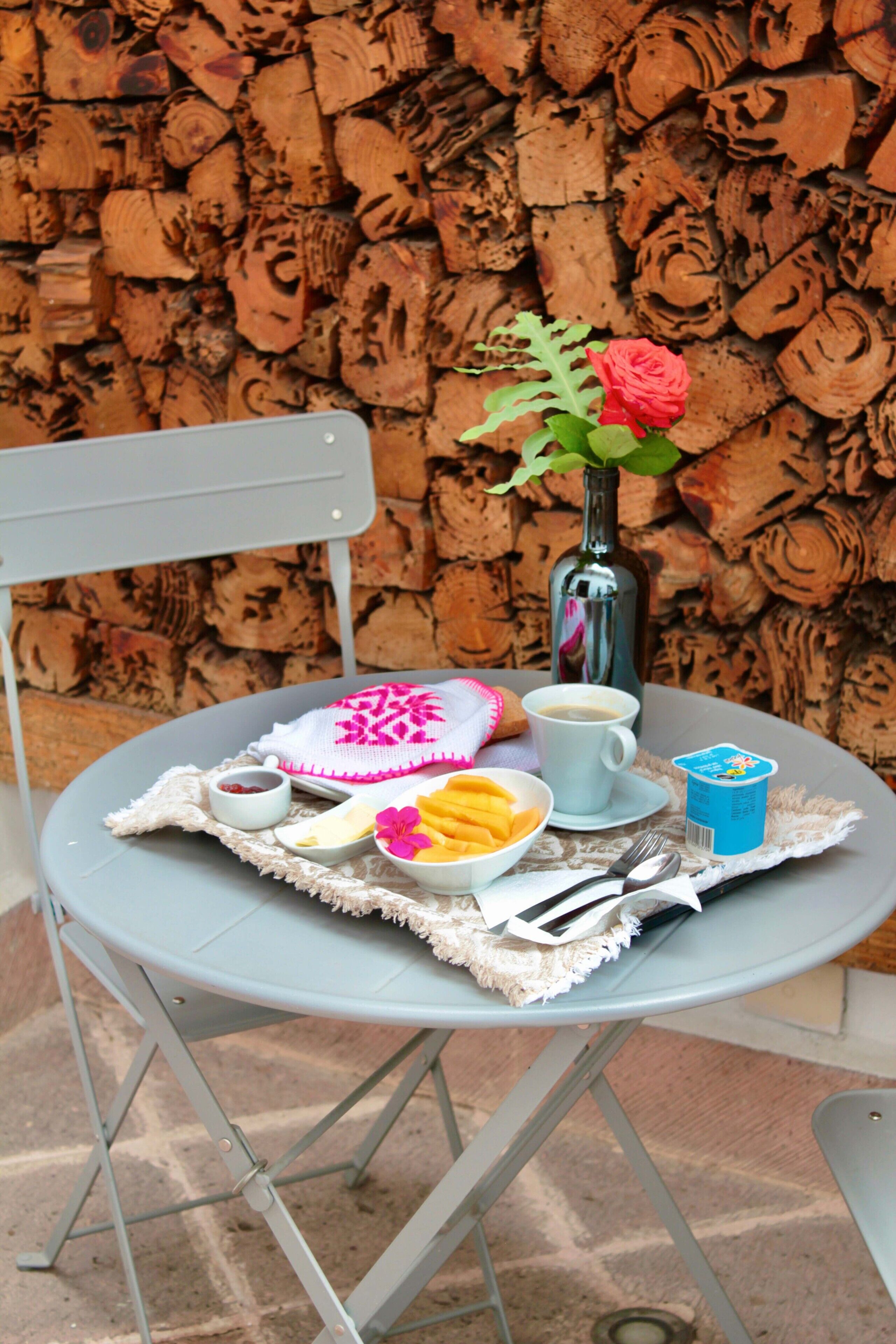 Une table dressée avec une assiette de nourriture, une tasse de café, un vase avec une fleur et une bouteille.