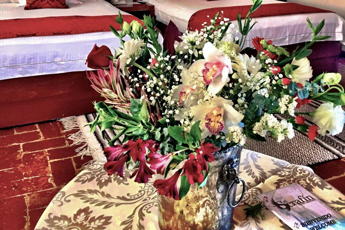 A hotel room with two beds, a floral arrangement on the floor, and a sign reading "el Serafin Hotel Boutique".