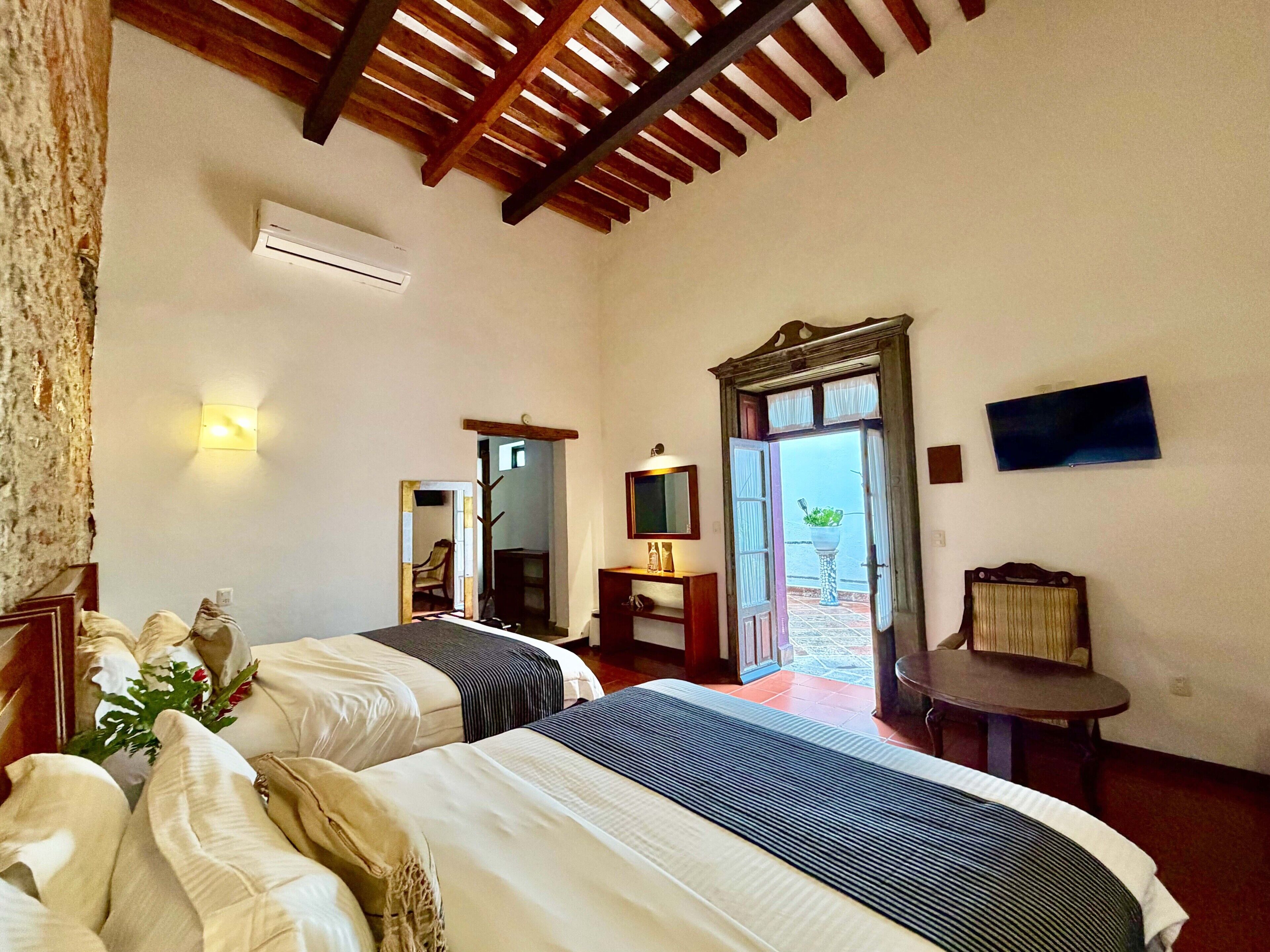 A hotel room with two beds, a television, a small table, and a balcony door.
