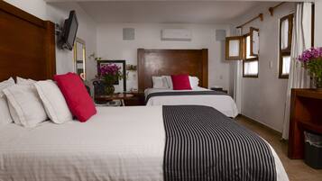 Ein Hotelzimmer mit zwei Betten, einem Fernseher, einer Klimaanlage und einem Schreibtisch mit Blumen.