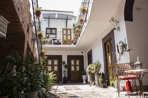 A courtyard with a wooden bench, potted plants, and a table with a red cushion.
