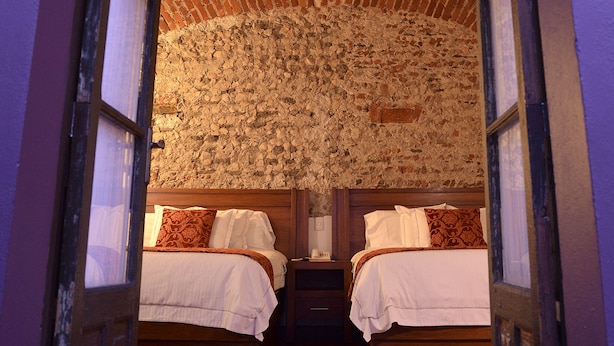 Una habitación con dos camas, una pared de ladrillo y techo de madera.