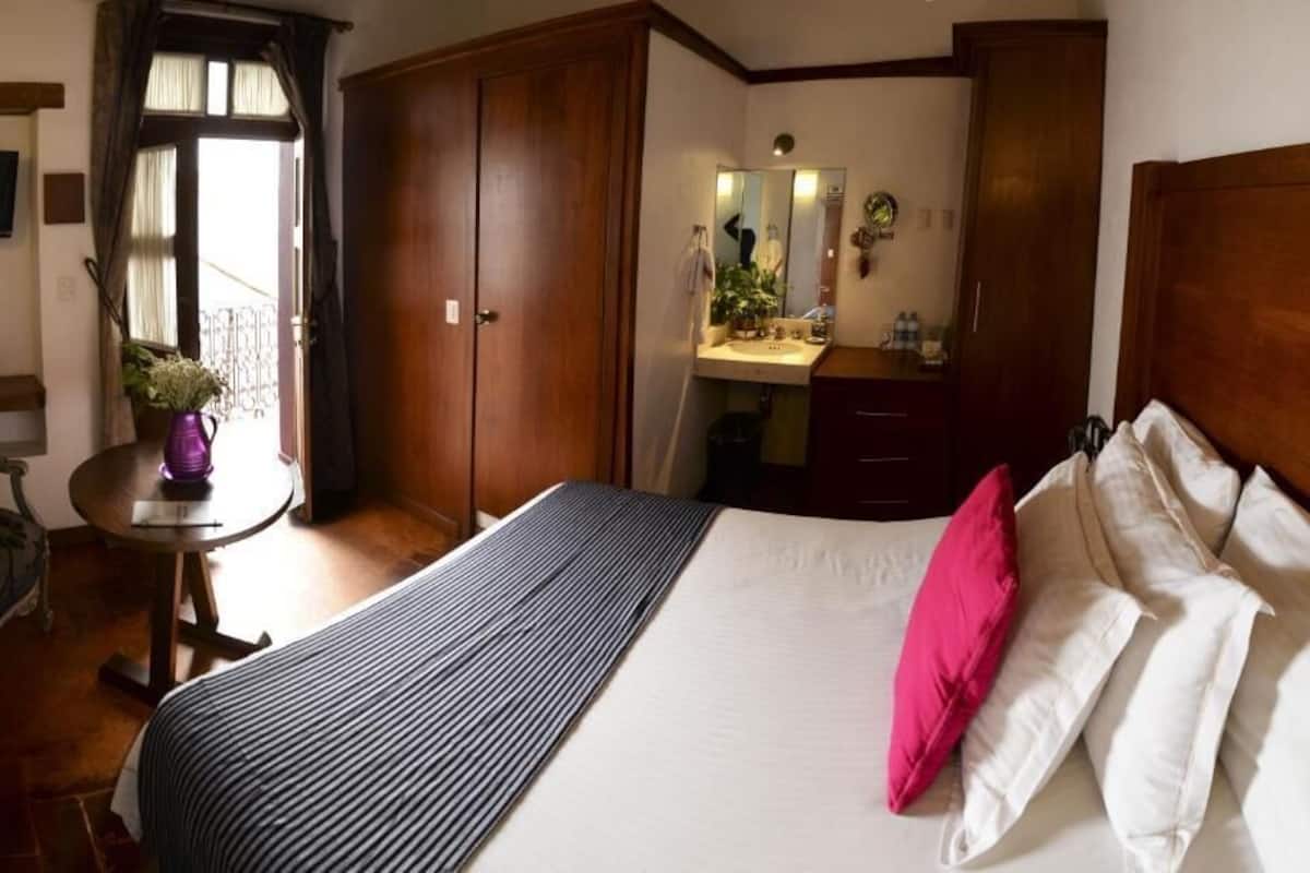 A hotel room with a bed, a desk, a chair, a wardrobe, a bathroom with a mirror, and a TV on the wall.
