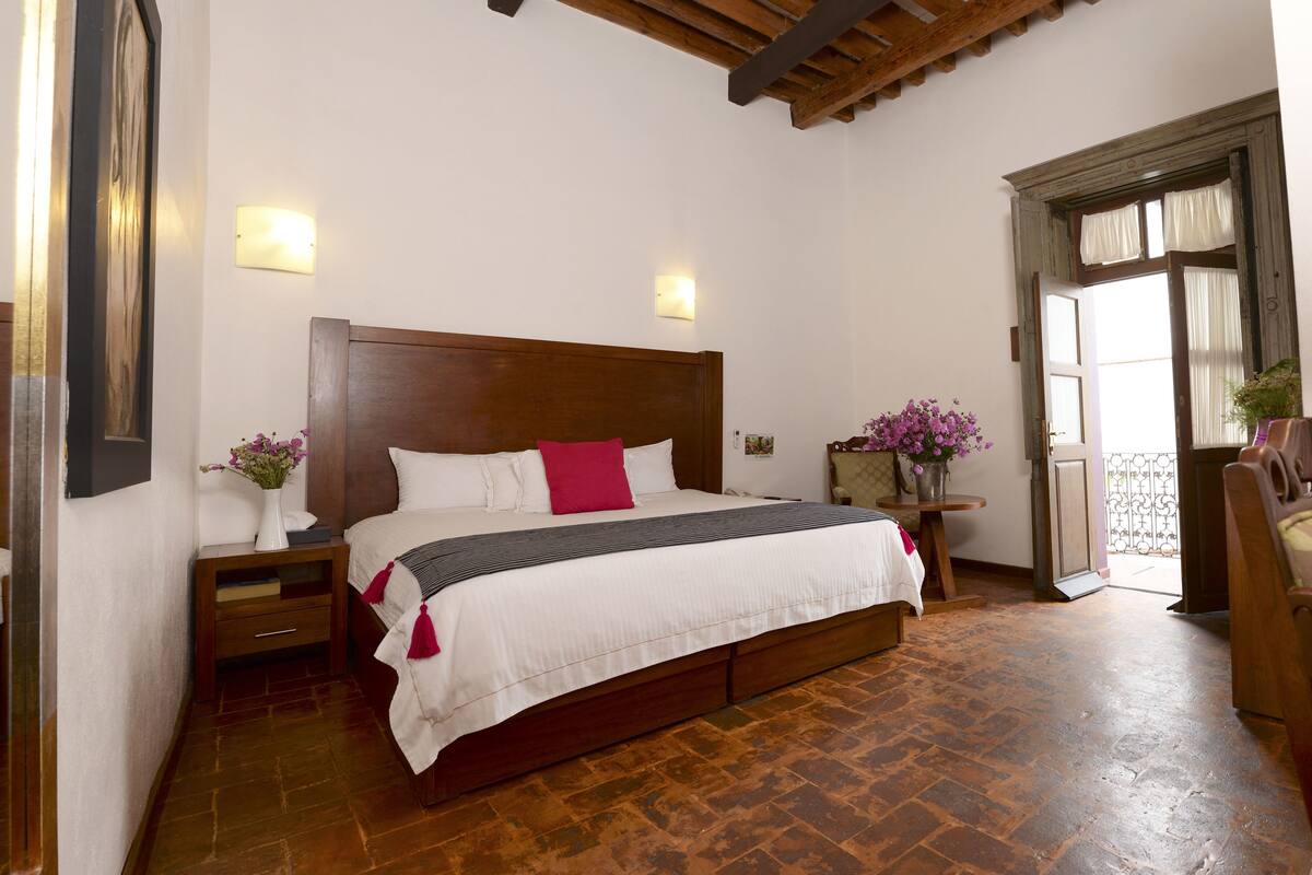 A bedroom with a wooden bed, white bedding, a nightstand with a vase of flowers, and a view of the outside balcony.