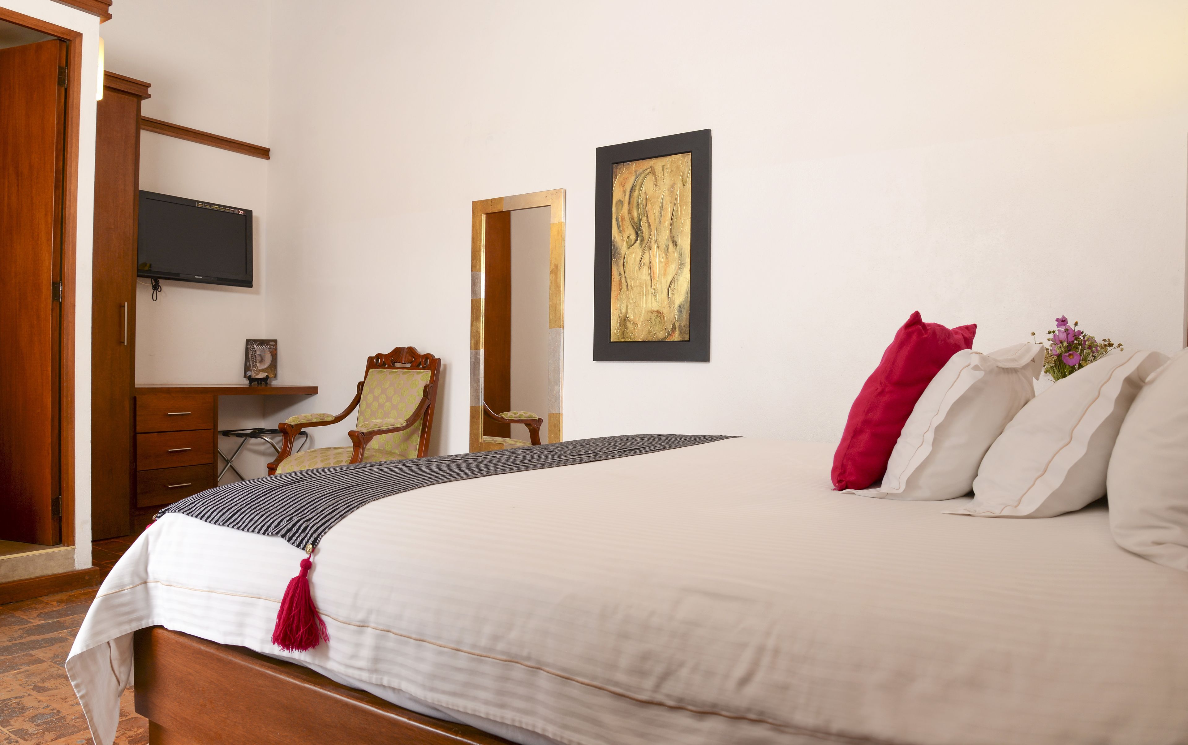A bedroom with a bed, a chair, a desk, a television, and a framed artwork on the wall.