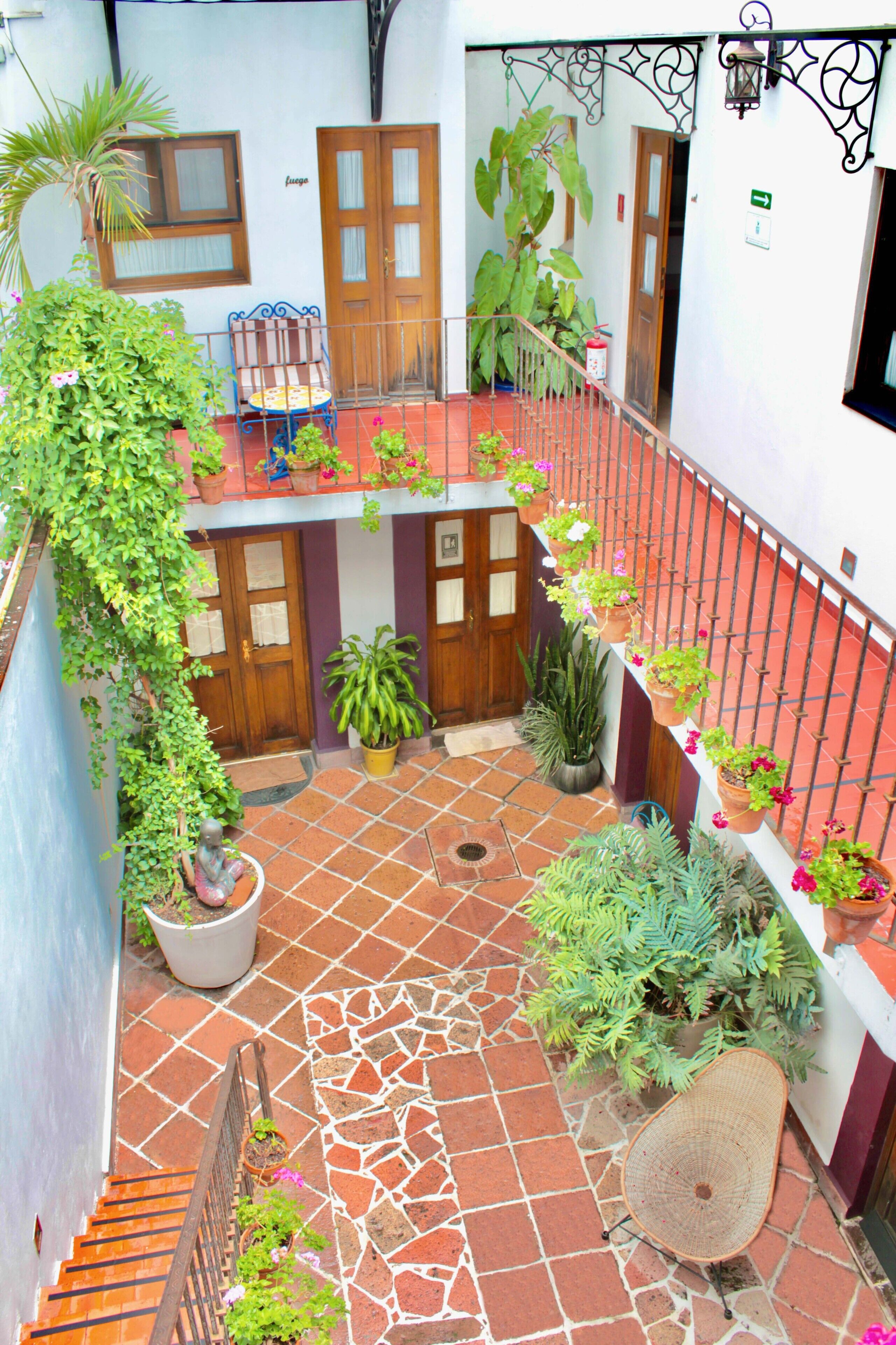 Un patio con suelo de baldosas, plantas en macetas, un banco de madera y una barandilla de metal.