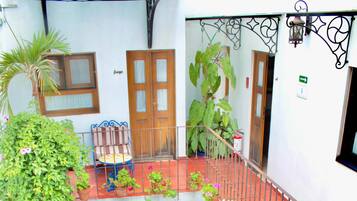 Un patio con suelo de baldosas, plantas en macetas, un banco de madera y una barandilla de metal.