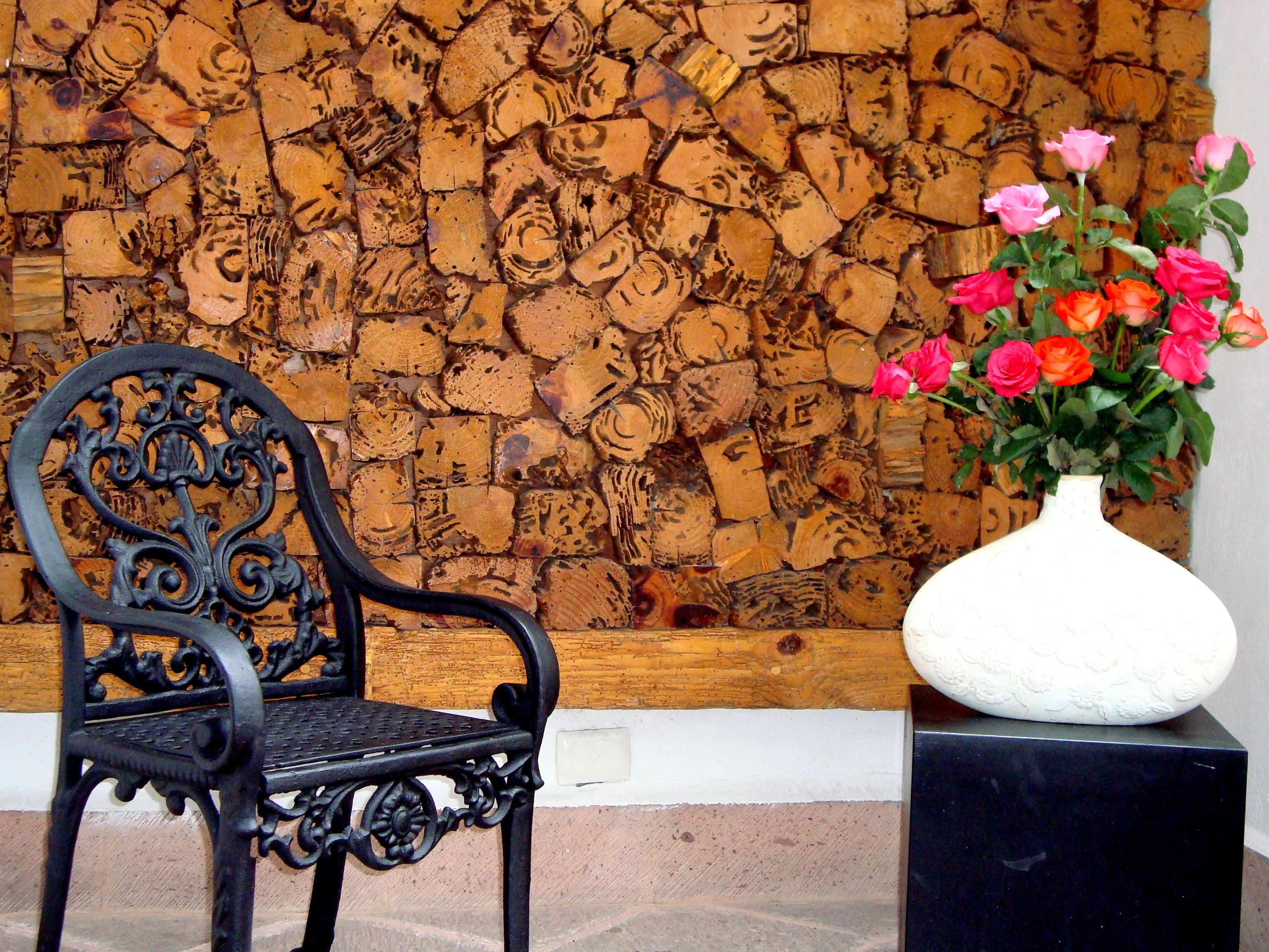 A black ornate chair, a white vase with pink and orange flowers, and a wall covered with wooden planks.