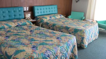 Habitación de hotel con dos camas, cada una con colcha estampada de flores, cabecero de madera, mesita de noche con lámpara y un cuadro en la pared.