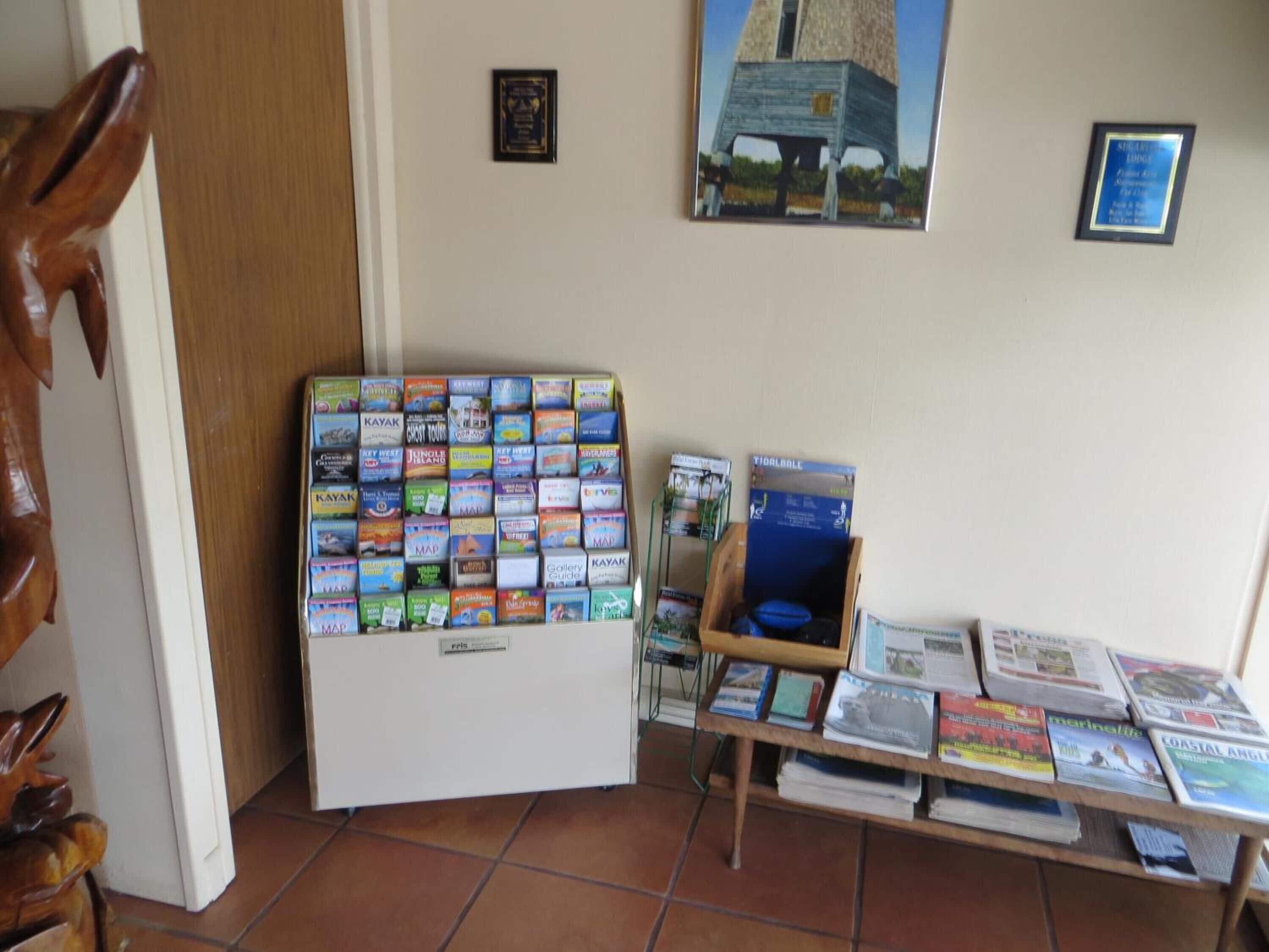 A room with a wall-mounted bookcase filled with travel guides, a small wooden table with additional books, and a door on the left.