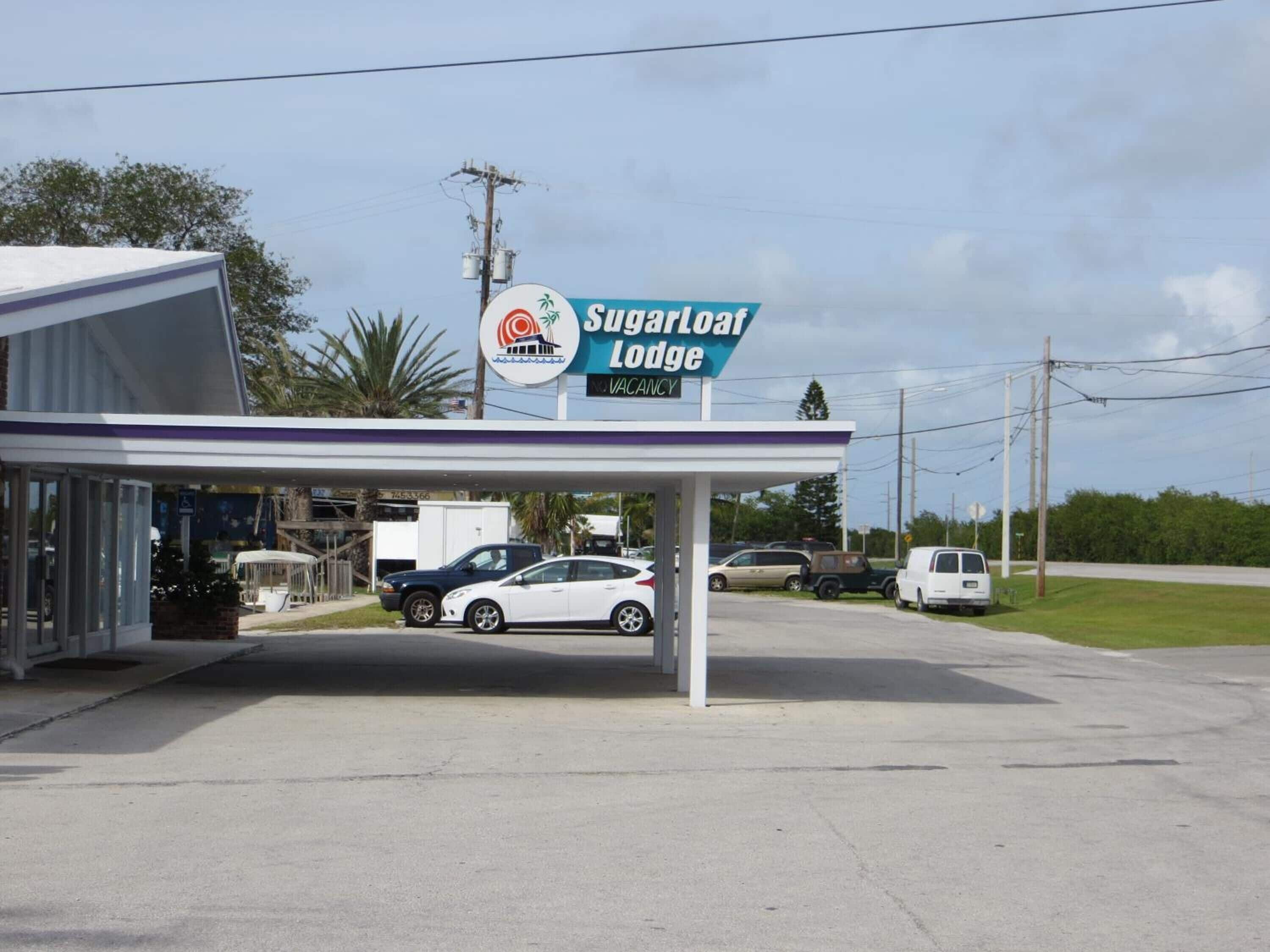 Une station-service appelée « Sugarloaf Lodge », dotée d’un espace de stationnement couvert et d’un bâtiment à la façade blanche.