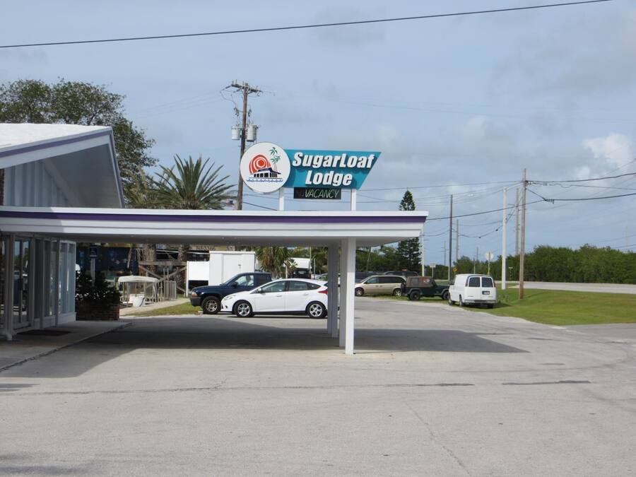 Une station-service appelée « Sugarloaf Lodge », dotée d’un espace de stationnement couvert et d’un bâtiment à la façade blanche.