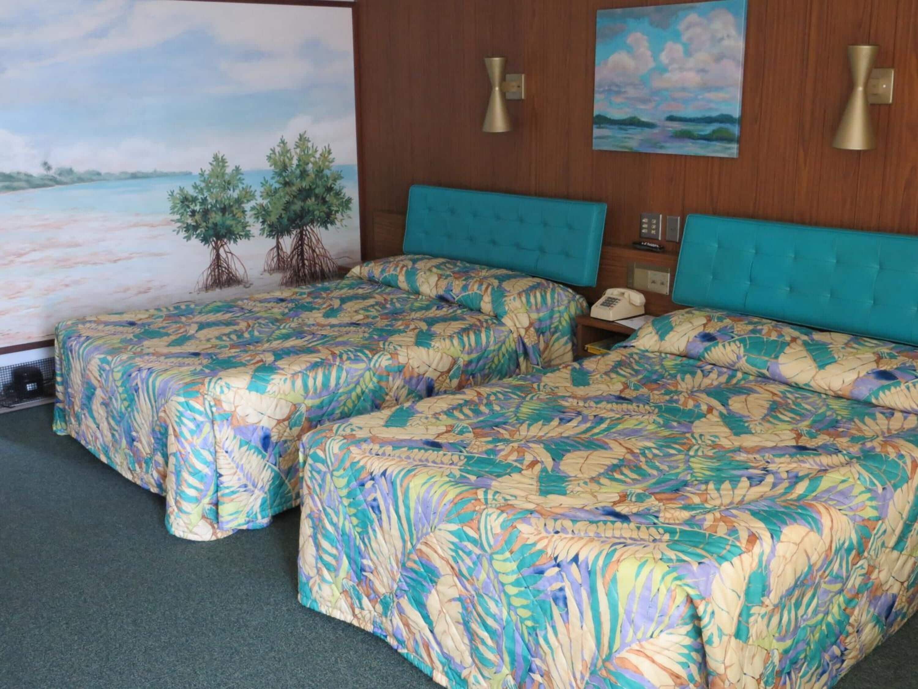 Ein Hotelzimmer mit zwei Betten, einem großen Gemälde einer Strandlandschaft und einer kleinen Zimmerpflanze.