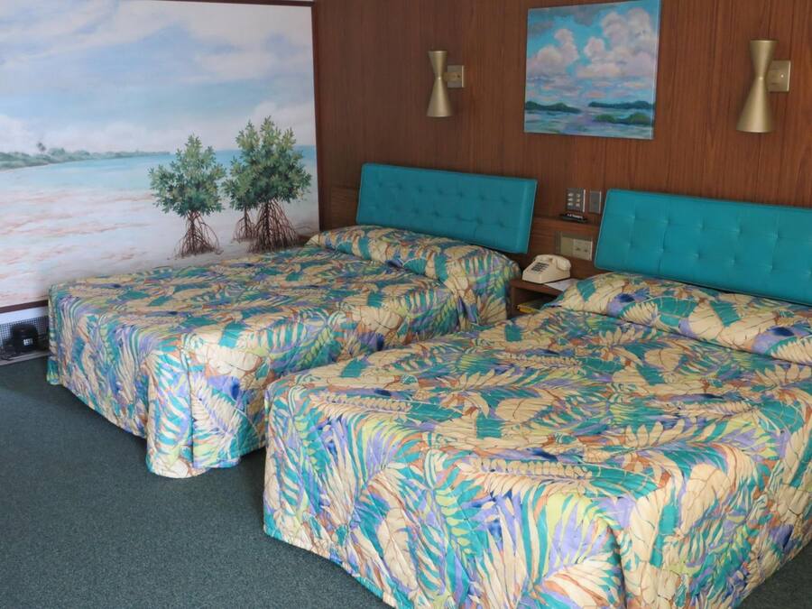 A hotel room with two beds, a large painting of a beach scene, and a small tree decoration.