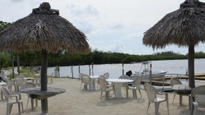 Un espace de restauration aménagé sur la plage, avec des parasols en chaume, des chaises et des tables en plastique blanc.