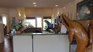Un espace d’accueil agrémenté d’une sculpture en bois, d’un comptoir de réception, d’un ordinateur et d’un téléviseur.