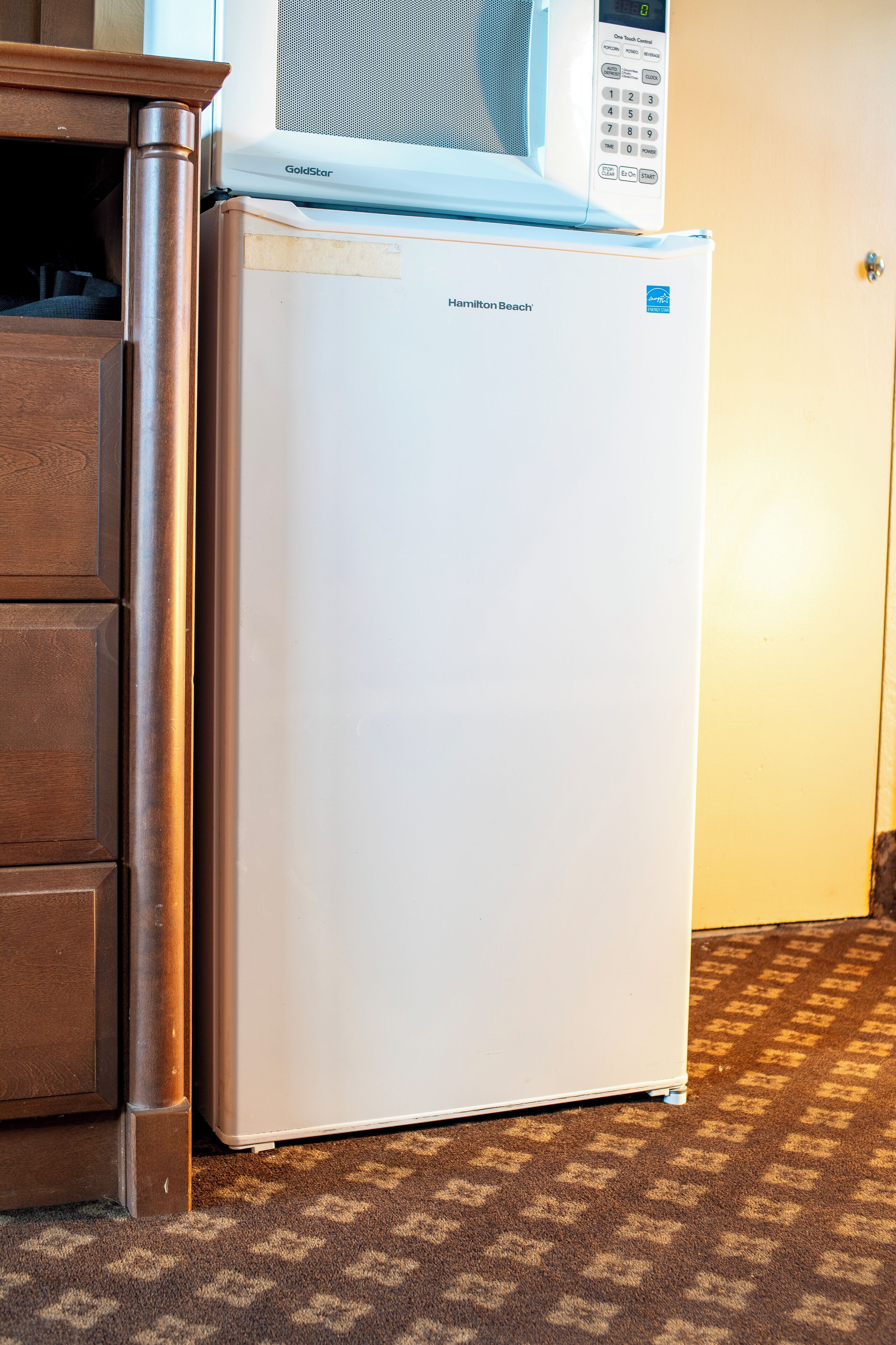 A white refrigerator with a digital display and a microwave on top, next to a wooden cabinet.