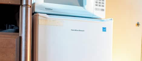 Un refrigerador blanco con pantalla digital y un microondas encima, junto a un mueble de madera.
