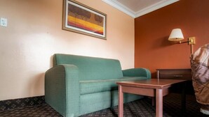 Una habitación con un sofá verde, una mesita de madera, una lámpara y un cuadro en la pared.
