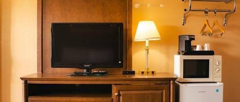 Ein Hotelzimmer mit einem Holztisch, einem Fernseher, einer Lampe, einer Mikrowelle und einem kleinen Kühlschrank.