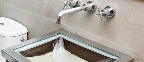 A modern bathroom with a glass sink, a chrome faucet, and a toilet.