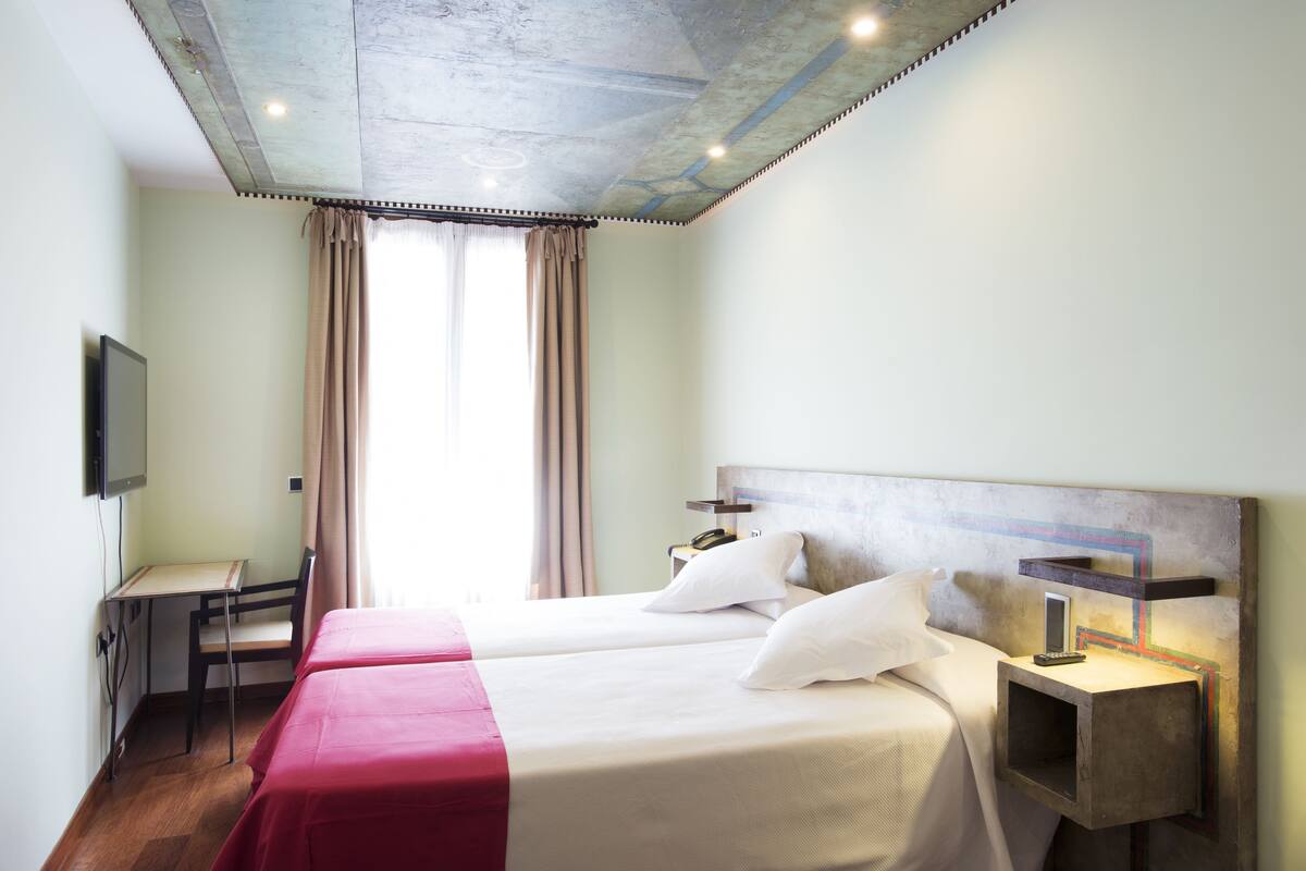 Una habitación de hotel con dos camas, un escritorio, una silla, un televisor y una mesita de noche con lámpara.