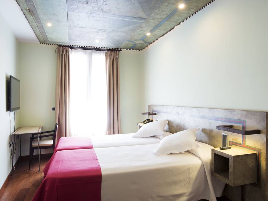 Una habitación de hotel con dos camas, un escritorio, una silla, un televisor y una mesita de noche con lámpara.
