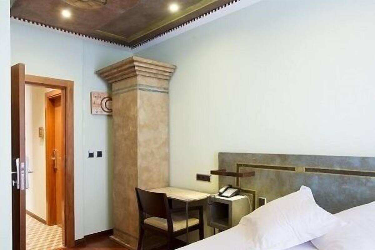 Habitación de hotel con cama, escritorio, silla y una mesita con teléfono.