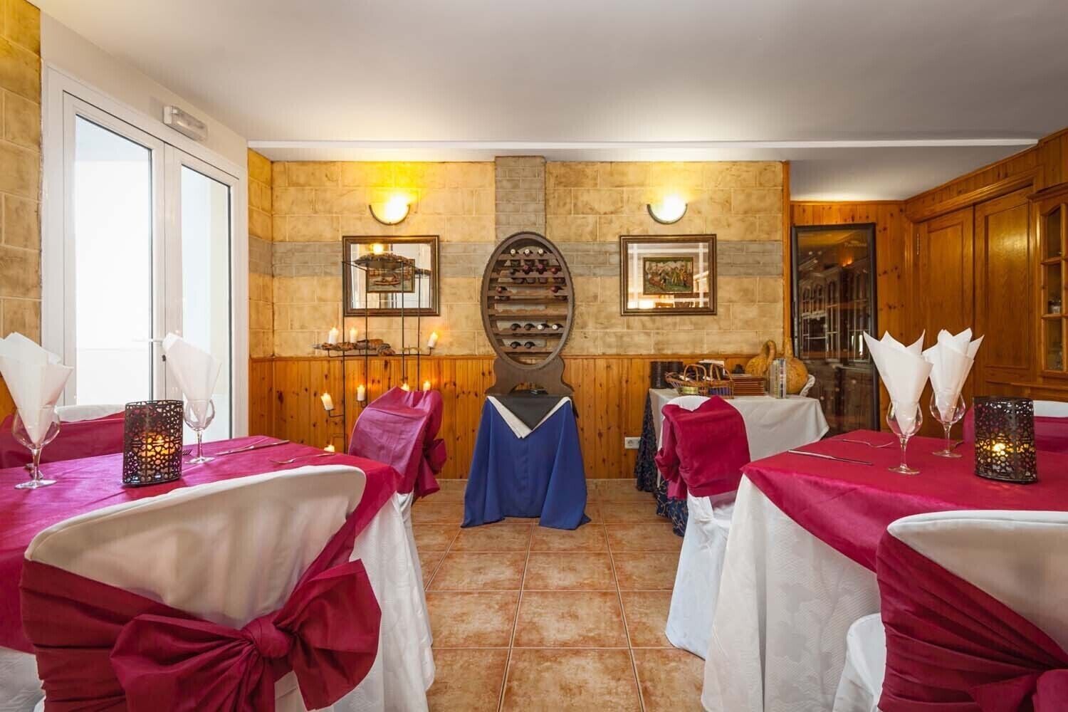 Comedor con mesas dispuestas para una comida, destacando una pared de piedra con cuadros enmarcados y un mueble de madera.