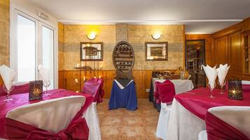 Comedor con mesas dispuestas para una comida, destacando una pared de piedra con cuadros enmarcados y un mueble de madera.