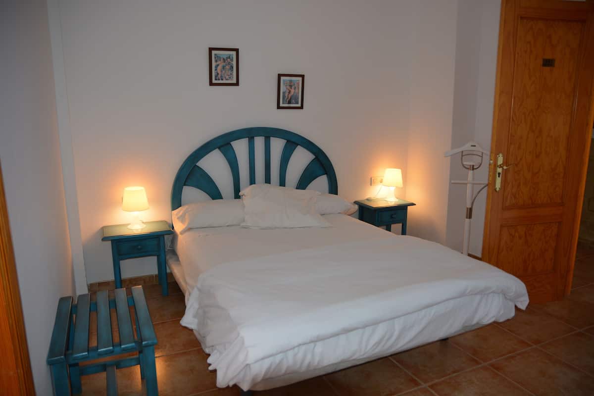 A neatly made bed with white bedding, two bedside tables with lamps, and a wooden door.