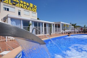 A hotel with a swimming pool, a water feature, and a clear blue sky.