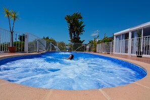 A hot tub with a person in it, surrounded by a white fence and palm trees. - Hotel Al Andalus (Nerja)