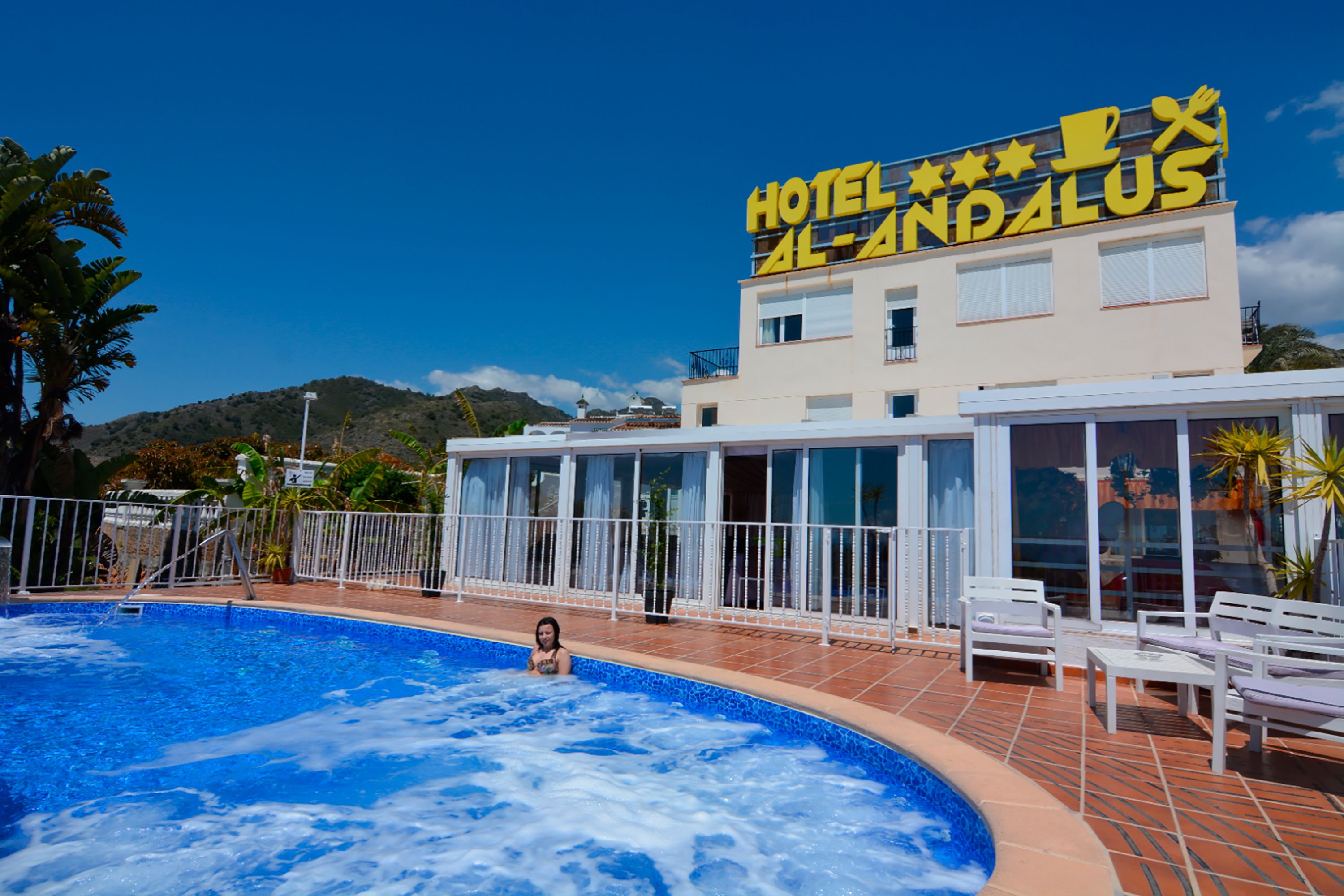 Un hôtel doté d'une piscine, d'une enseigne indiquant « HÔTEL AL ANDALUS », et ayant une chaîne de montagnes en arrière-plan.
