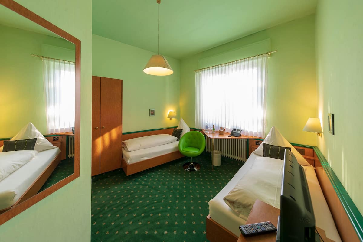 Et hotelværelse med to senge, en grøn stol, et skrivebord med lampe og et fjernsyn.