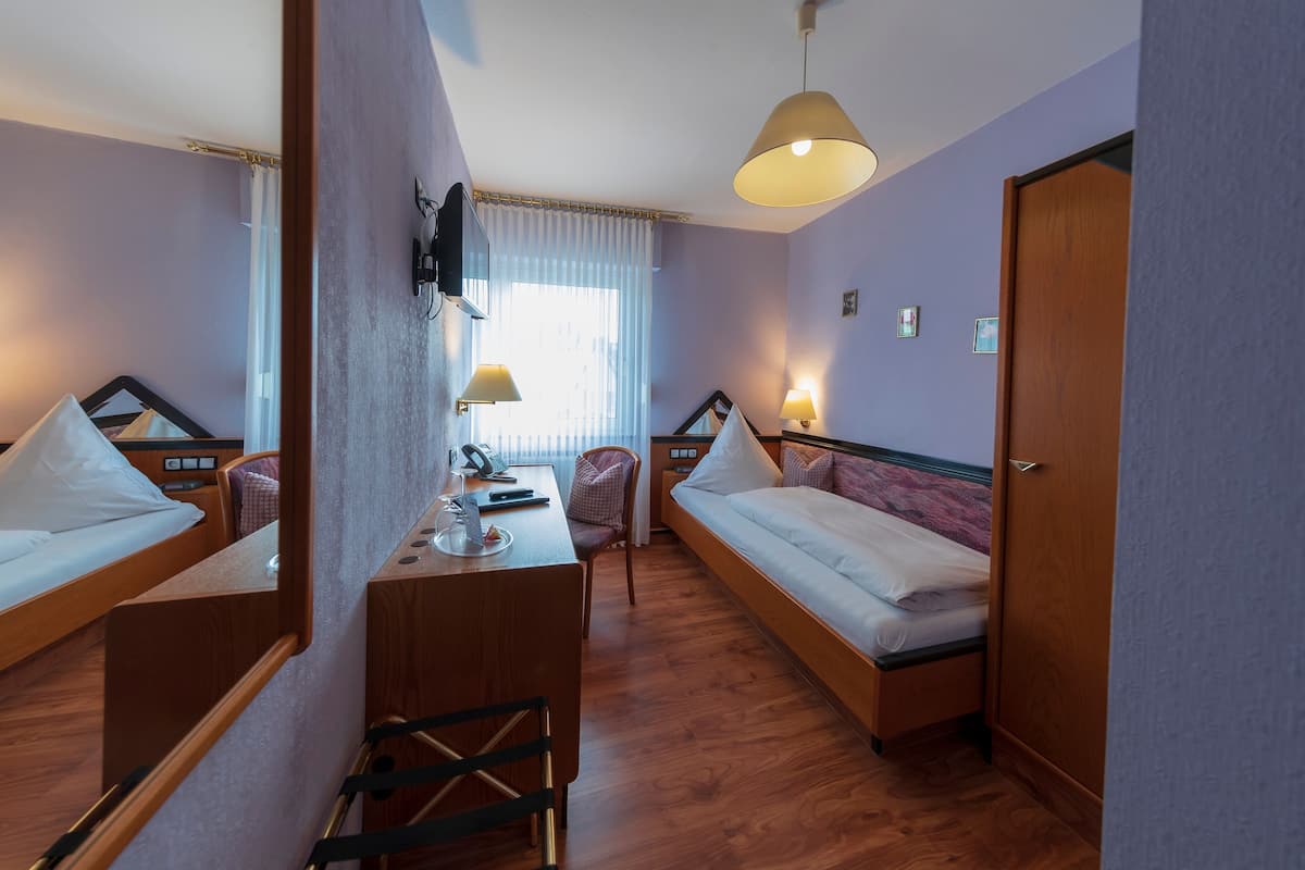 Et hotelværelse med to senge, et skrivebord med stol, et fjernsyn og en lampe.