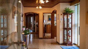 A hotel lobby with a reception desk, a wooden cabinet with glass doors, and a blue mat with text. - Hotel Höhn (Ruedesheim am Rhein)