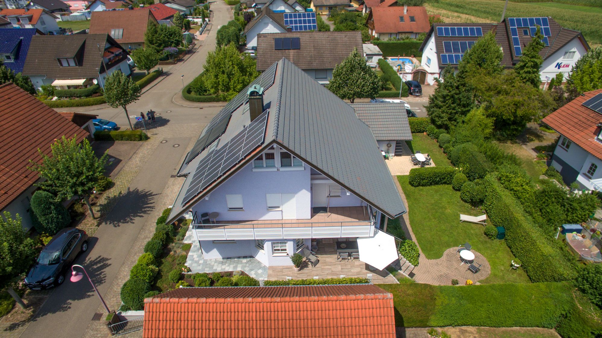 Une maison d’habitation avec un toit en pente, des panneaux solaires et un jardin bien entretenu.