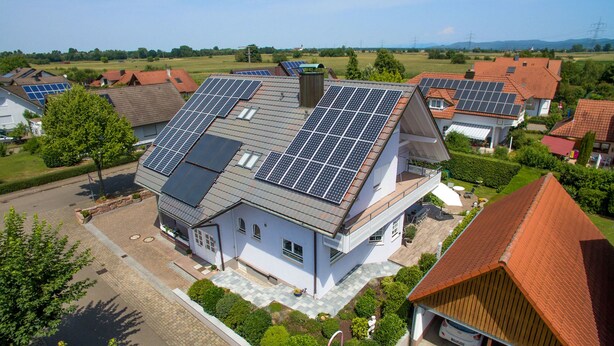 A house with multiple solar panels on the roof, surrounded by greenery and other houses. - Gästehaus Alba (Rust)