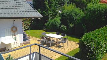 A patio area with a table and chairs, solar panels on the roof, and a garden with trees and shrubs.