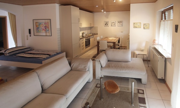A compact living space with a sofa, a small table, a kitchenette, and a dining area.