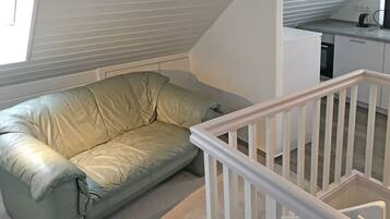 A room with a green leather sofa, a white staircase, and a kitchen area.
